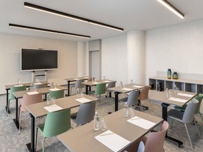 A modern conference room with tables, chairs, a flat-screen TV, and a shelf with decorative items. - Mercure Sofia City  (Sofia)