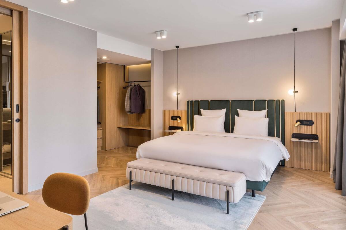 Una habitación de hotel moderna con una cama grande, mesitas de noche, un banco y un escritorio con una silla.