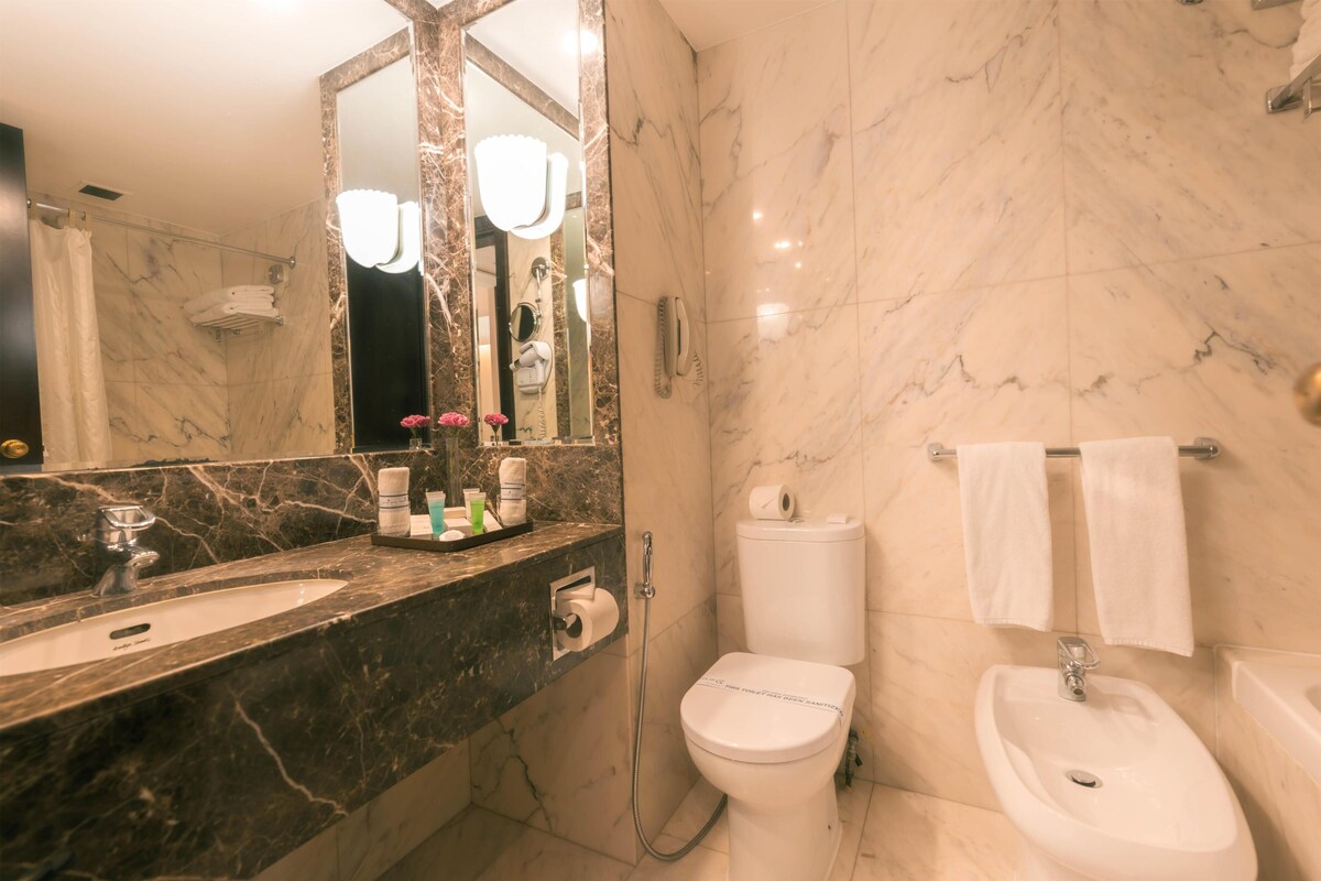 Een moderne badkamer met een marmeren wastafel, toilet, bidet en een grote spiegel met verlichting.