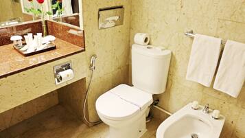 A bathroom with a toilet, bidet, sink, and a mirror with a rose vase.