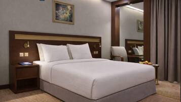 A hotel room with a large bed, a nightstand with a lamp, a chair, a mirror, and a painting on the wall.
