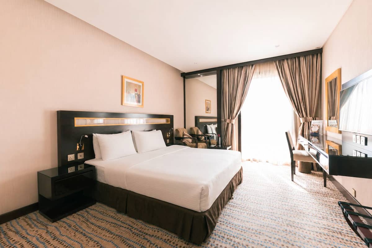 A hotel room with a large bed, bedside tables, a desk, a chair, a television, and a window with curtains.