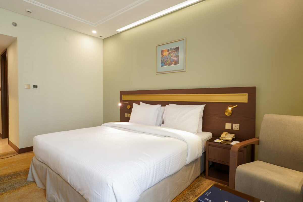 Een hotelkamer met een groot bed, een nachtkastje met telefoon en een stoel.