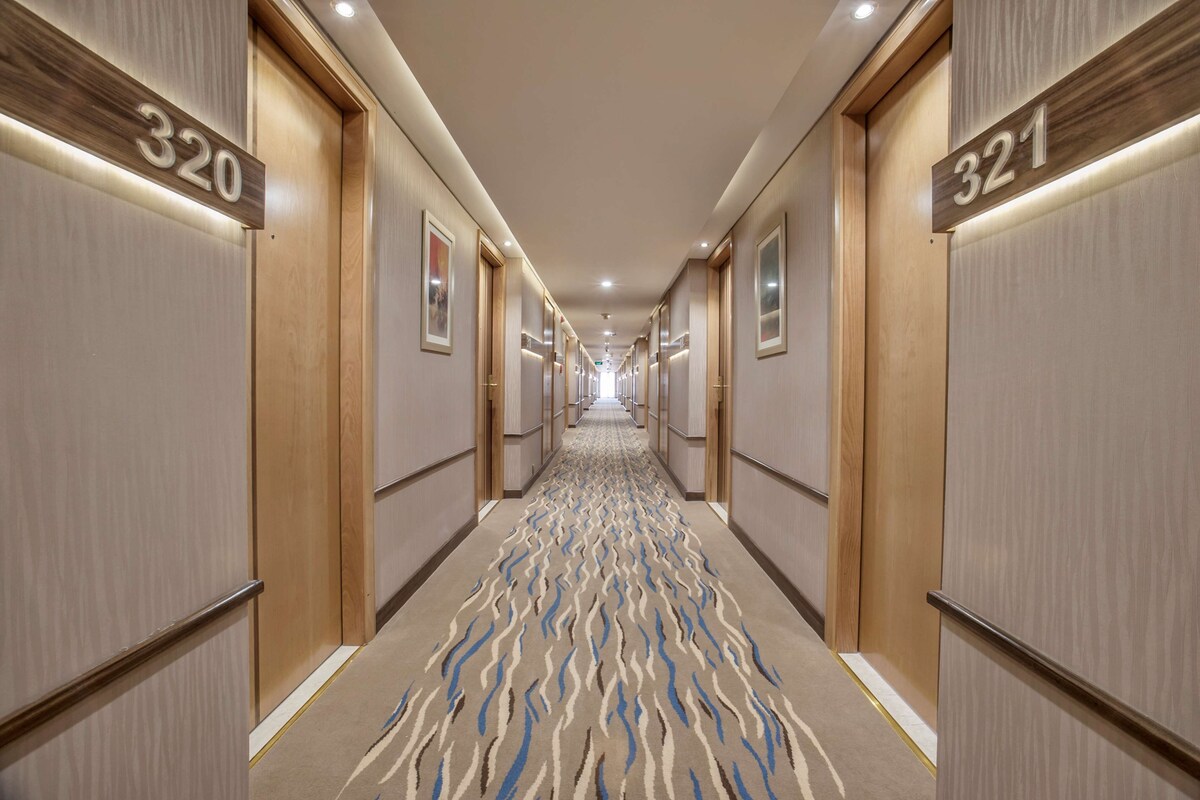Een hotelgangen met deuren genummerd 320 en 321, bekleed met een golvend tapijt en een plafond met inbouwspots.