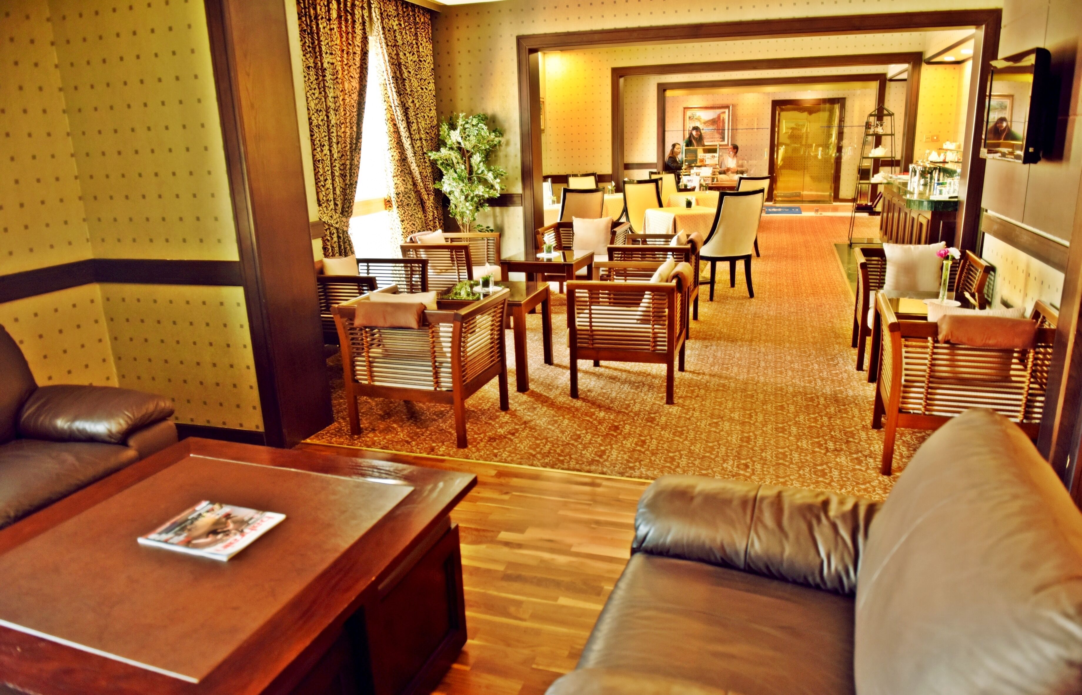 A hotel lobby with leather sofas, wooden tables, and a carpeted floor.