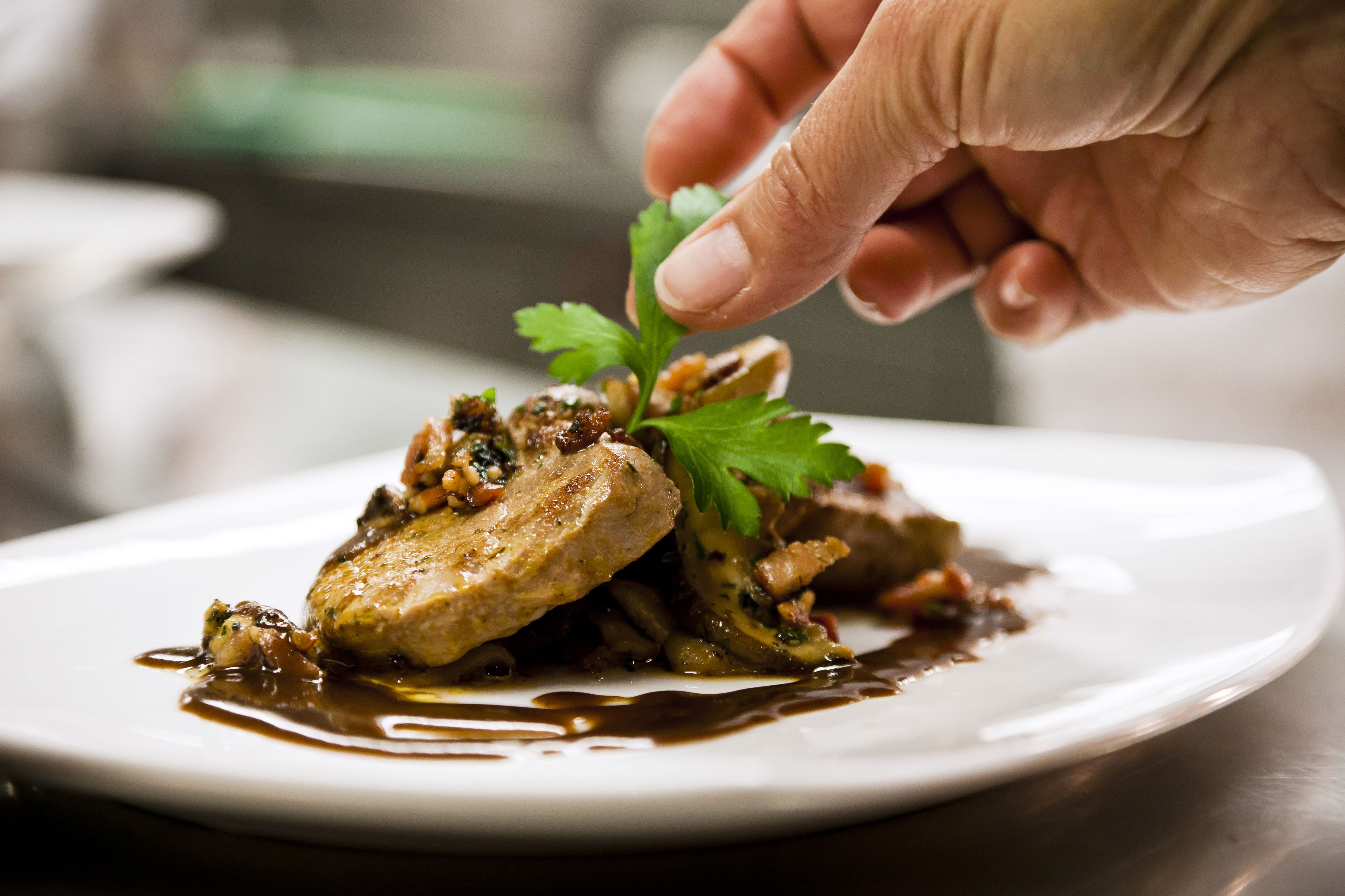 Une main qui dépose une garniture sur un plat.