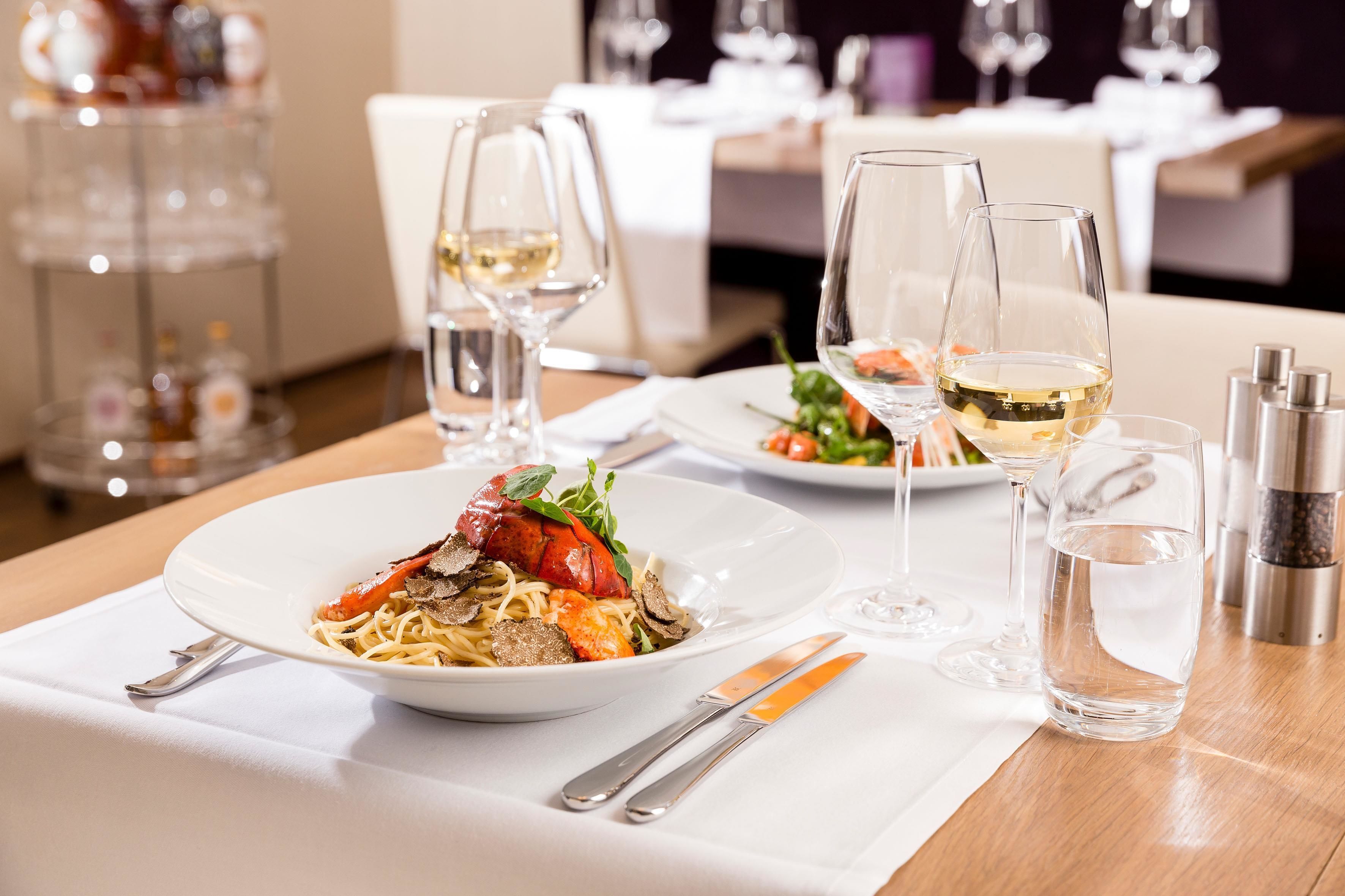 A dining table set with plates of food, wine glasses, and cutlery.