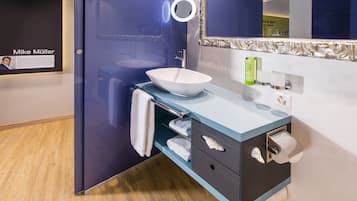 A modern bathroom with a large mirror, a white sink, and a towel rack.