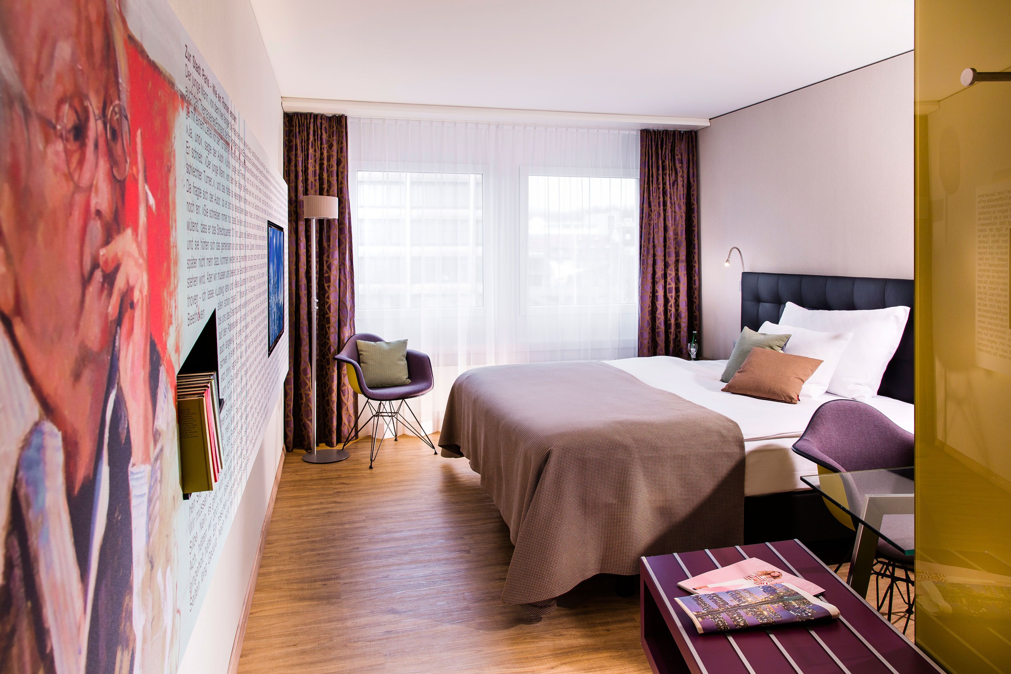 A hotel room with a large bed, a desk, a chair, and a wall with artwork.