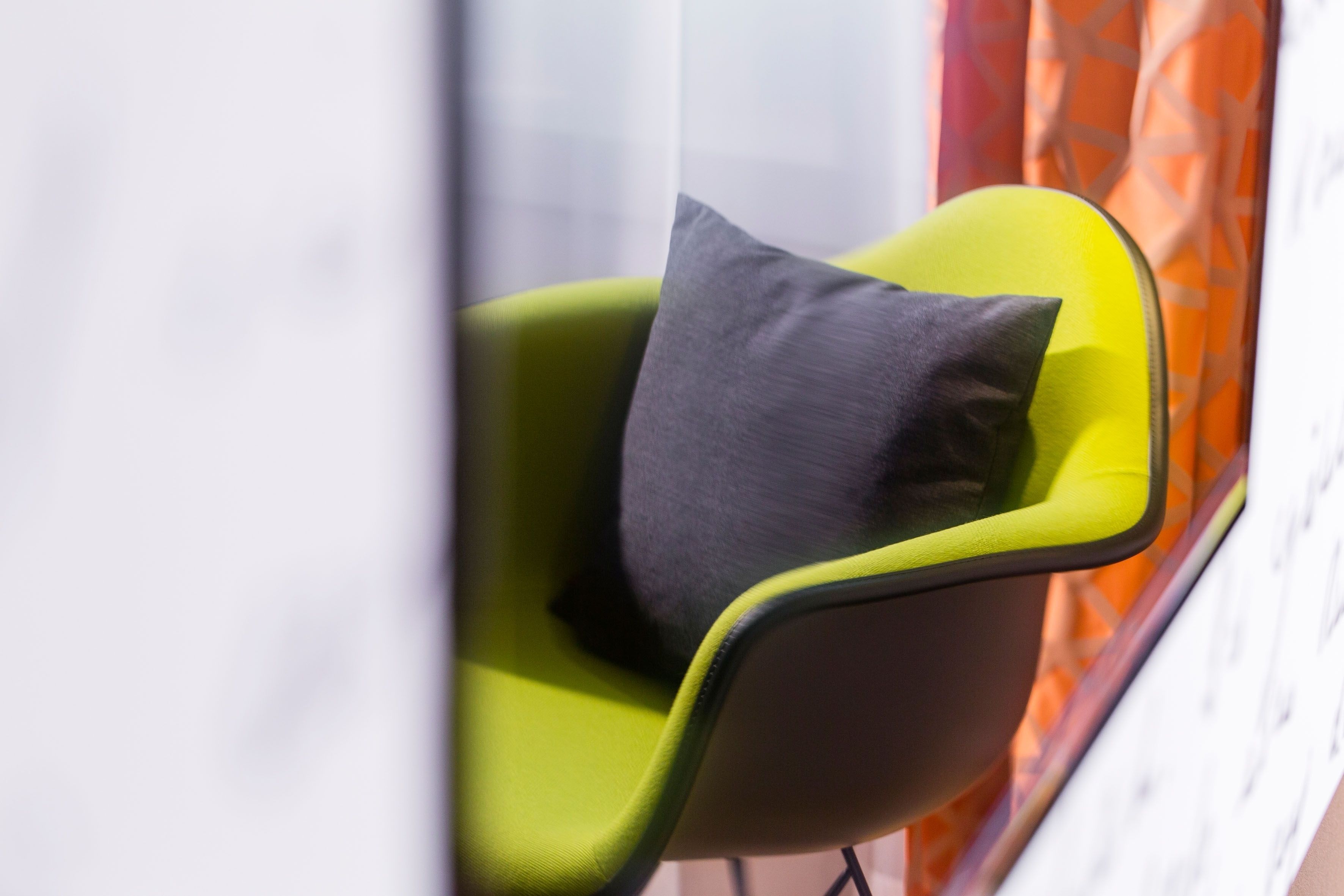 A modern chair with a dark cushion in a room with a patterned curtain.
