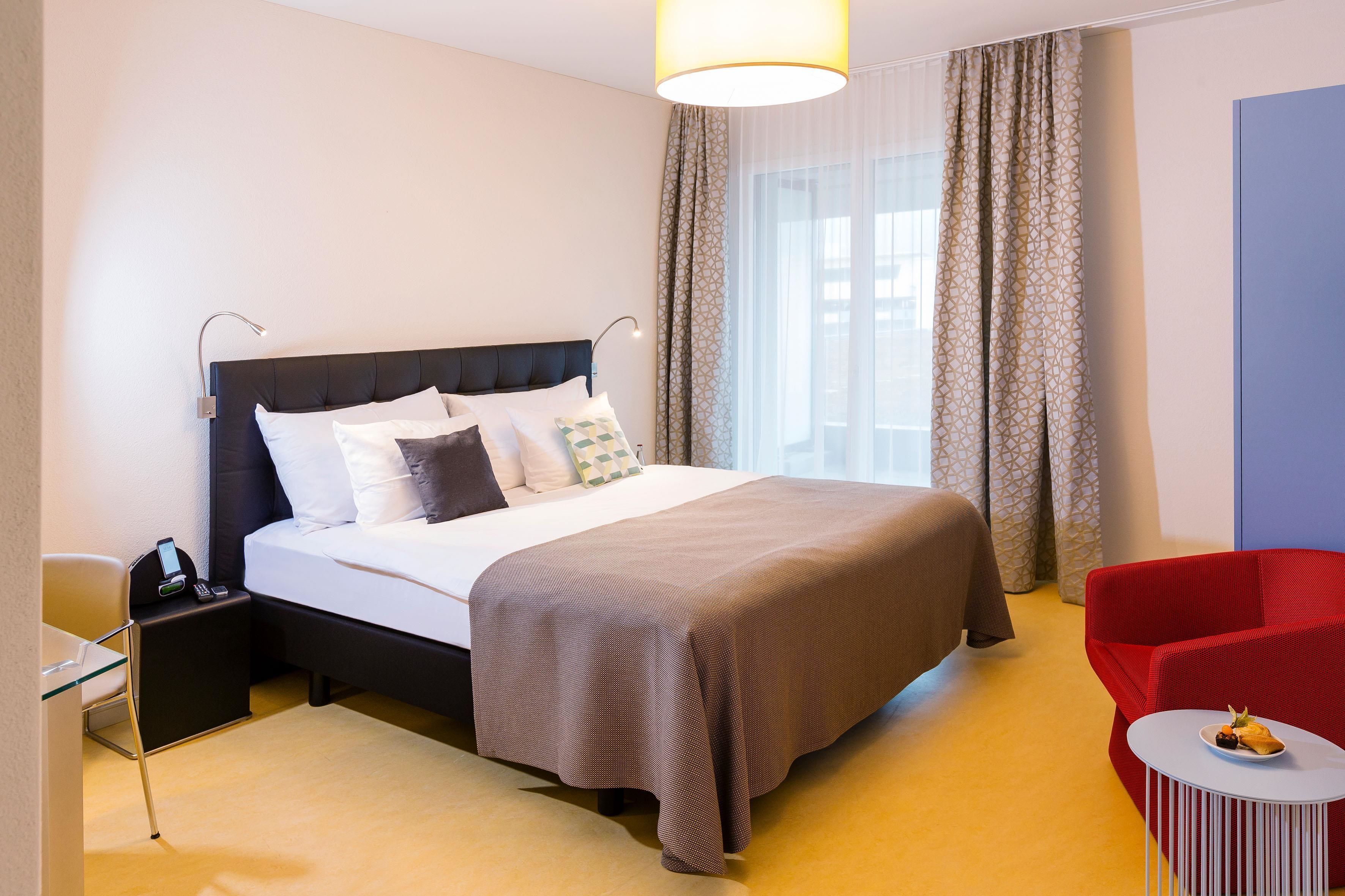 A hotel room with a bed, bedside table, chair, and a small table with a plate.