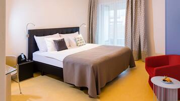 A hotel room with a bed, bedside table, chair, and a small table with a plate.