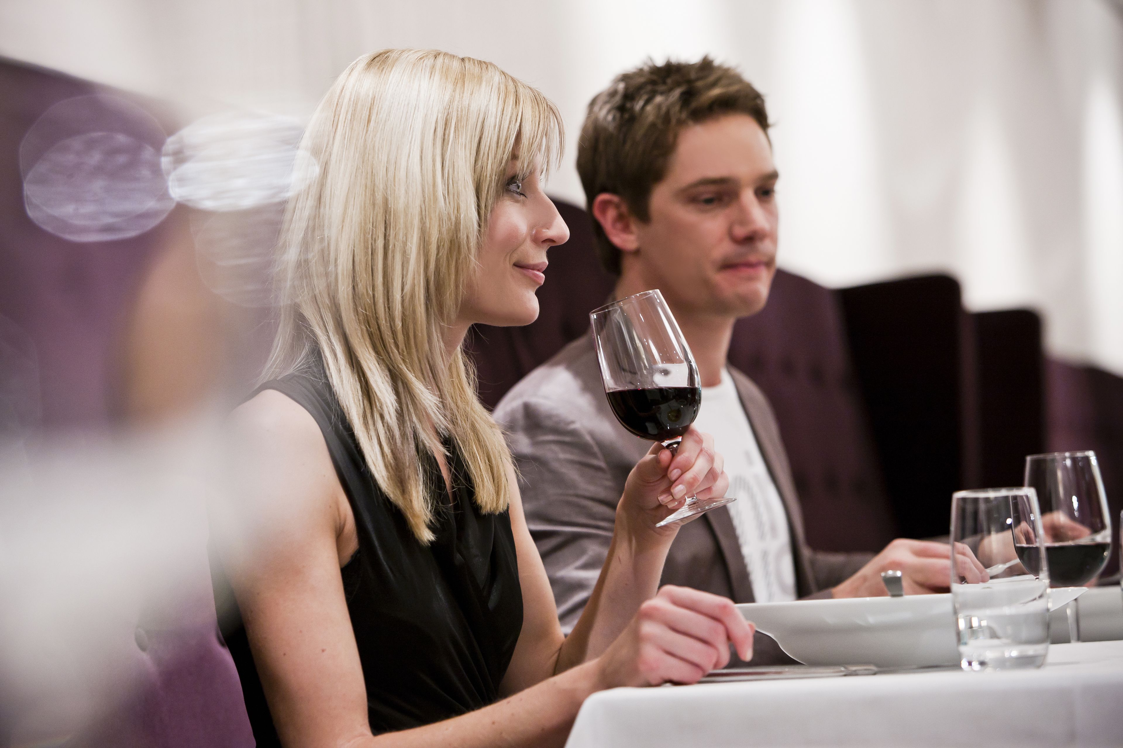 A person holding a wine glass at a table with other empty glasses and a laptop.
