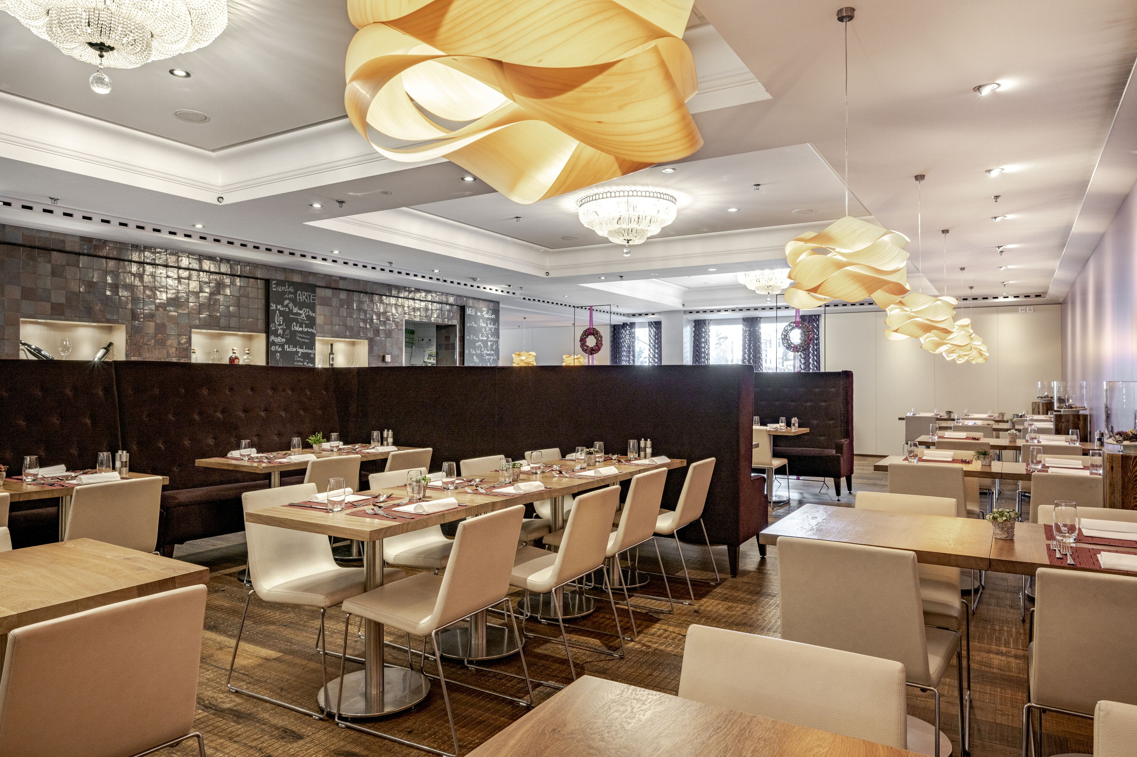 A modern restaurant with a long dining table, white chairs, and a chandelier.
