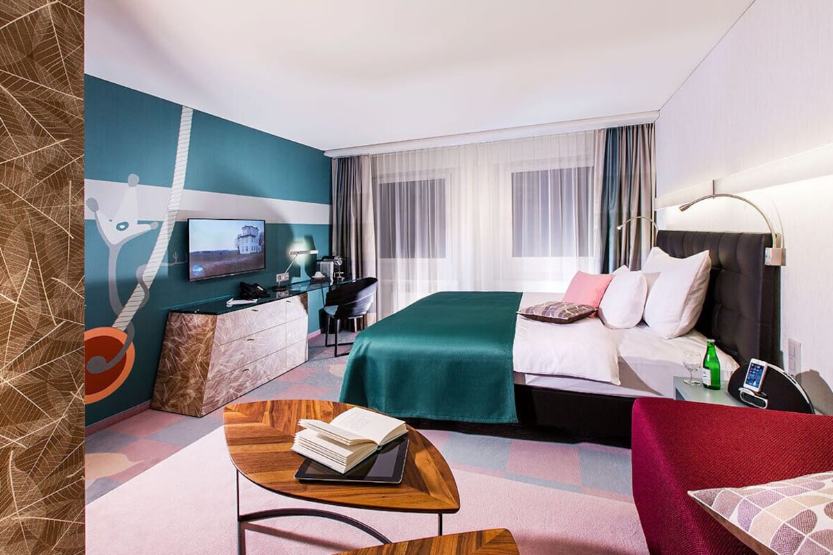 A hotel room with a bed, desk, TV, and a view of the outdoors.
