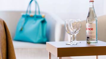 Eine klare Glasflasche Wasser, ein Glas und eine blaue Handtasche auf einem kleinen Tisch.