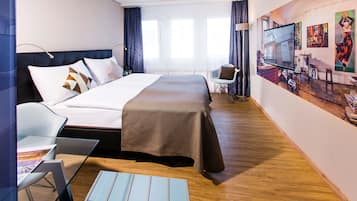 Habitación de hotel con una cama grande, un escritorio, una silla y un televisor en la pared.