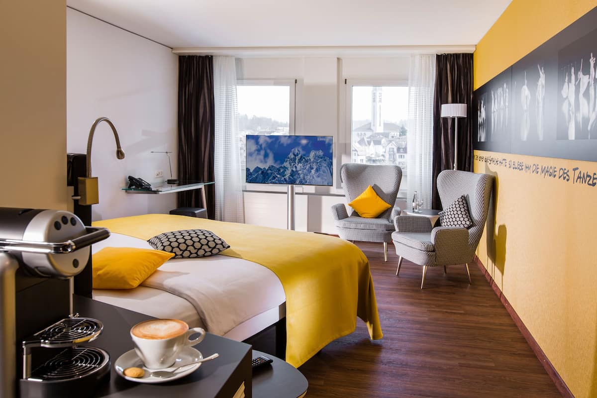 A hotel room with a bed, a coffee machine, a TV, and a chair.