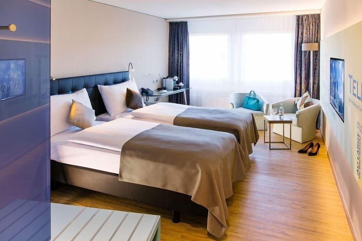 A hotel room with two beds, a desk with a computer, a chair, and a TV.