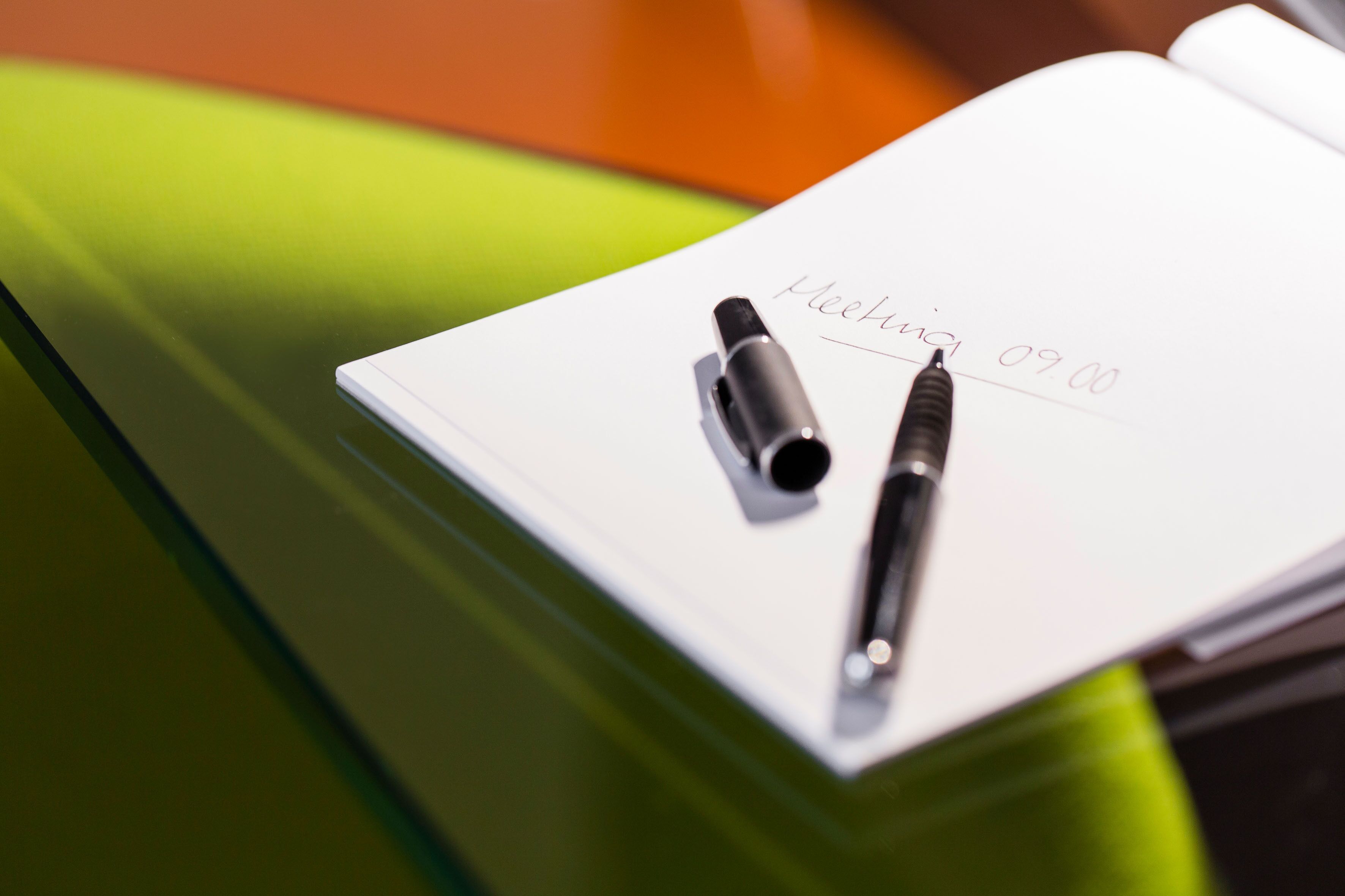 Ein Notizbuch mit einem Stift darauf, mit dem Text 'Meeting 09:00' auf der Seite.