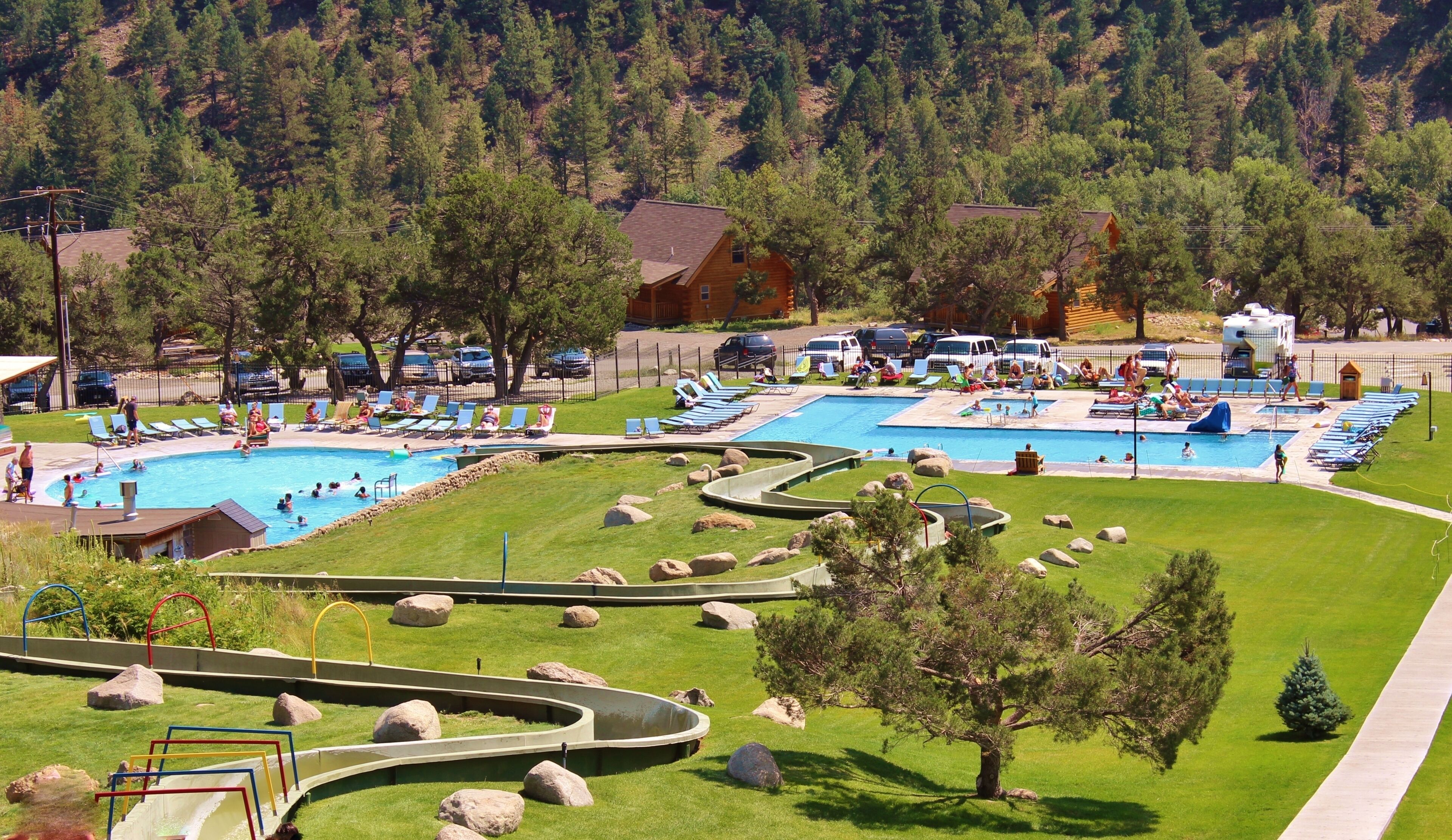 A resort with multiple swimming pools, lounge areas, and a scenic mountainous backdrop.