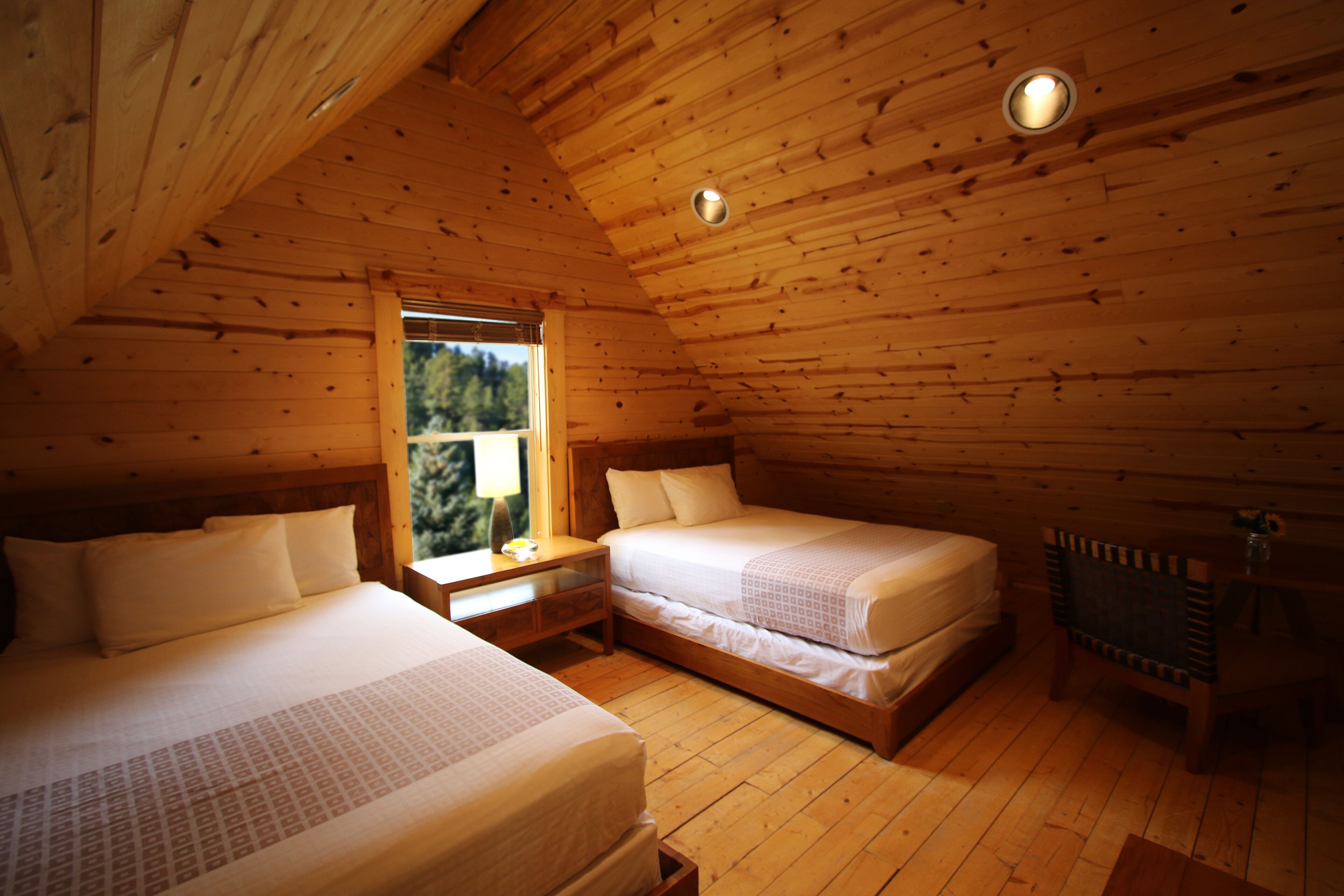 A cabin with two beds, wooden walls, a window, and a ceiling light.