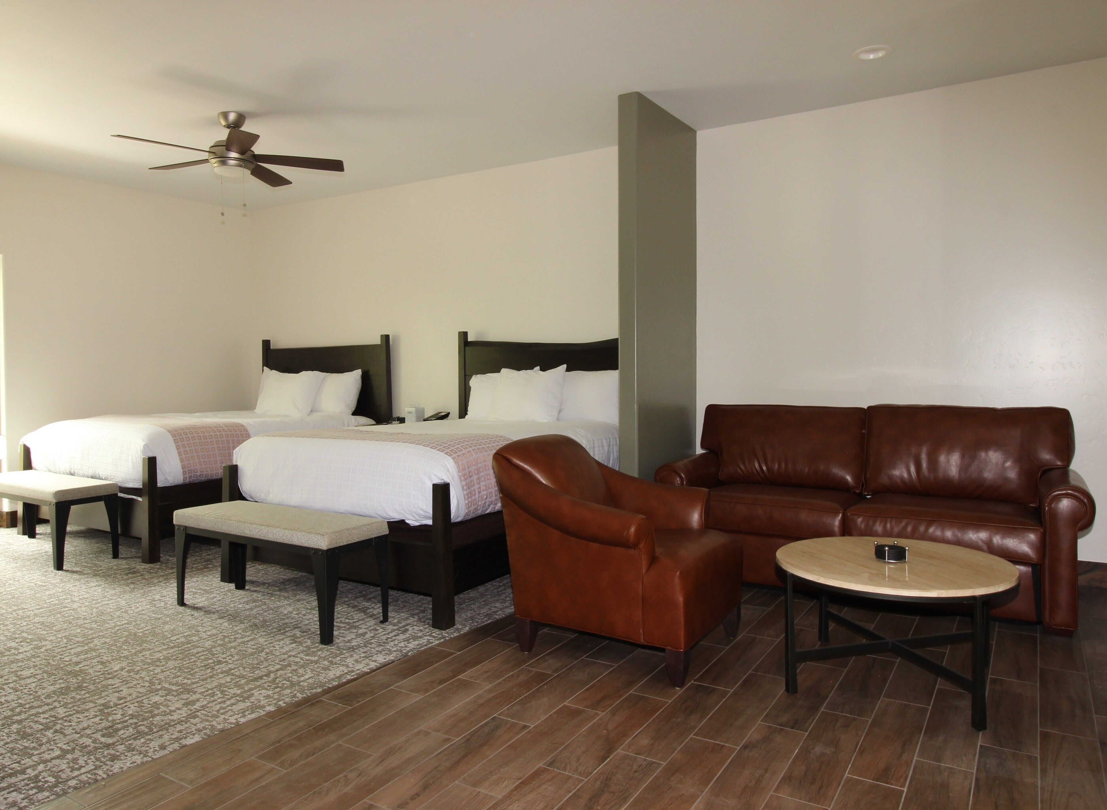 A hotel room with two beds, a brown leather sofa, a small round table, and a ceiling fan.