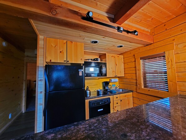 Una cocina compacta con gabinetes de madera, un refrigerador negro, un microondas y un lavamanos.