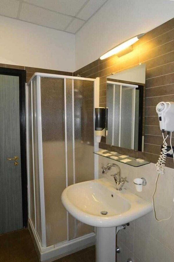 Un baño con cabina de ducha, lavamanos, espejo y secador de pelo.