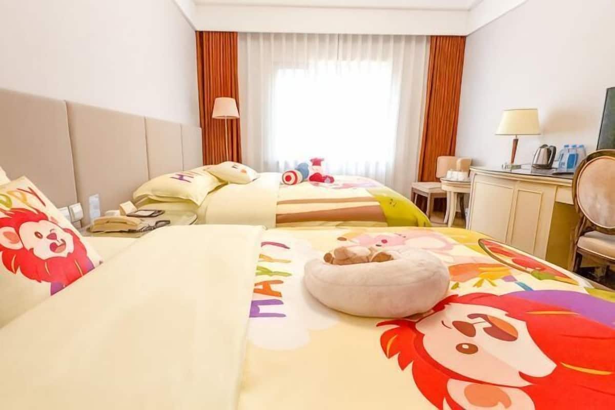 A hotel room with two beds, a desk, a chair, a lamp, and a window with curtains.