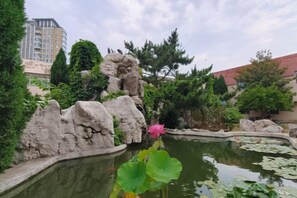 A landscaped garden with a pond, rocks, and a pink flower in the foreground. - Orient Haitian Guibin Hotel (Yantai)