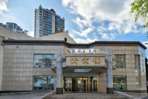 A hotel entrance with a sign, a set of double doors, and a tall building in the background. - Orient Haitian Guibin Hotel (Yantai)