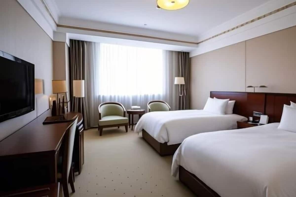 A hotel room with two beds, a TV, a desk, and a chair.