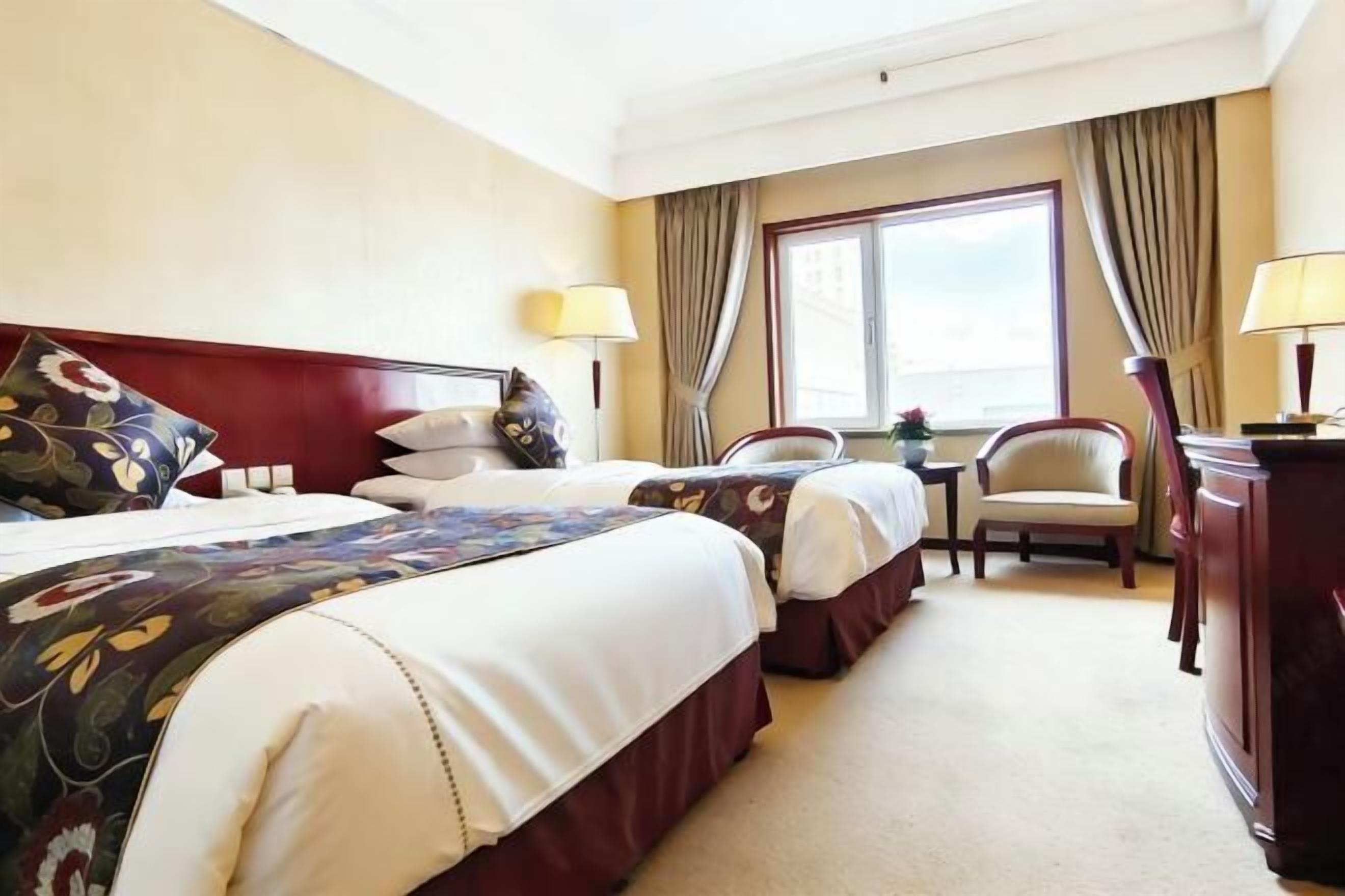 A hotel room with two beds, a desk, a chair, and a window with curtains.