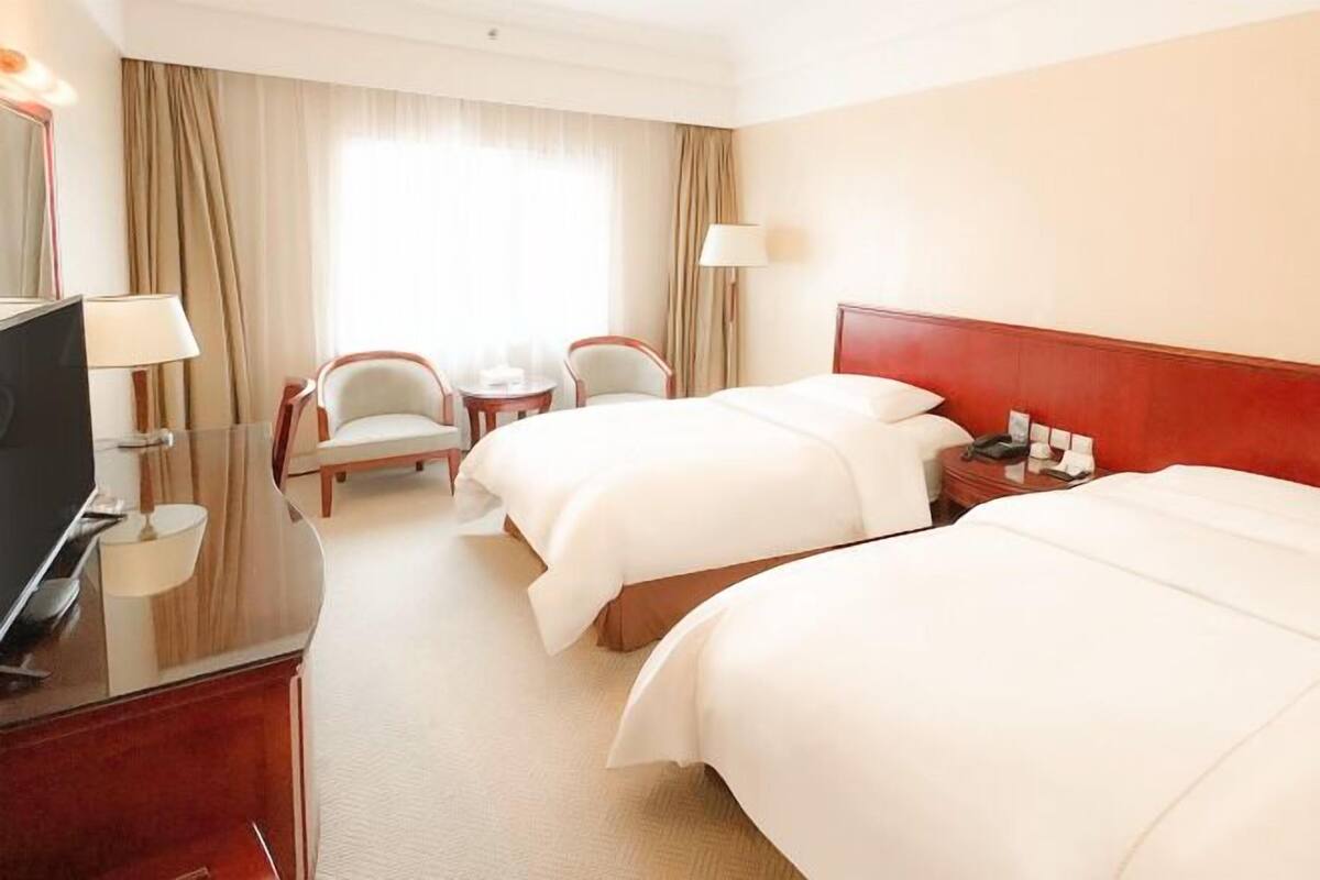 A hotel room with two beds, a TV, a desk, and a chair.