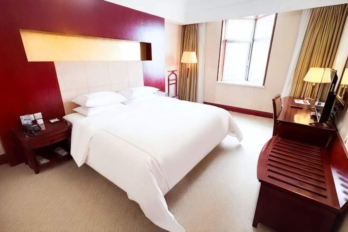 A hotel room with a large bed, a nightstand, a desk, and a chair.