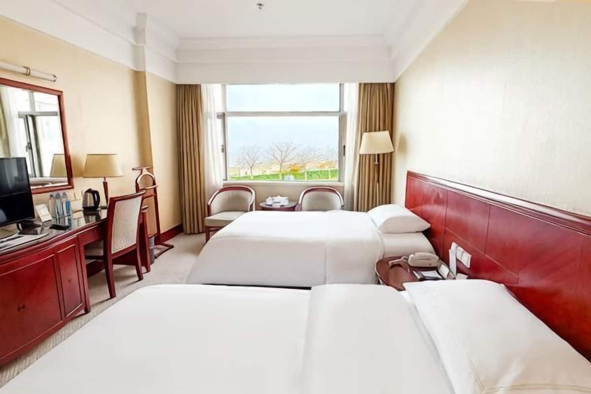 A hotel room with two beds, a desk with a chair, a television, and a window with a view.