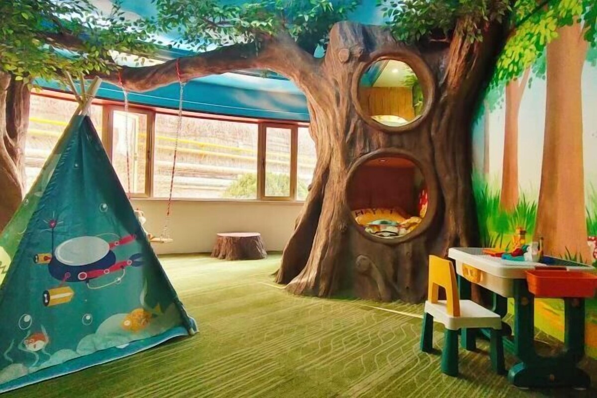 A room with a tree-themed play area, including a hanging tent, a treehouse, and a small table with chairs.