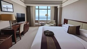 A hotel room with a large bed, a desk with a TV, a chair, a small table, and a window with a view. - Orient Haitian Guibin Hotel (Yantai)