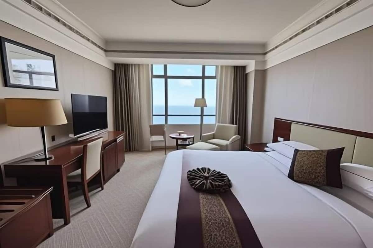 A hotel room with a large bed, a desk with a TV, a chair, a small table, and a window with a view.