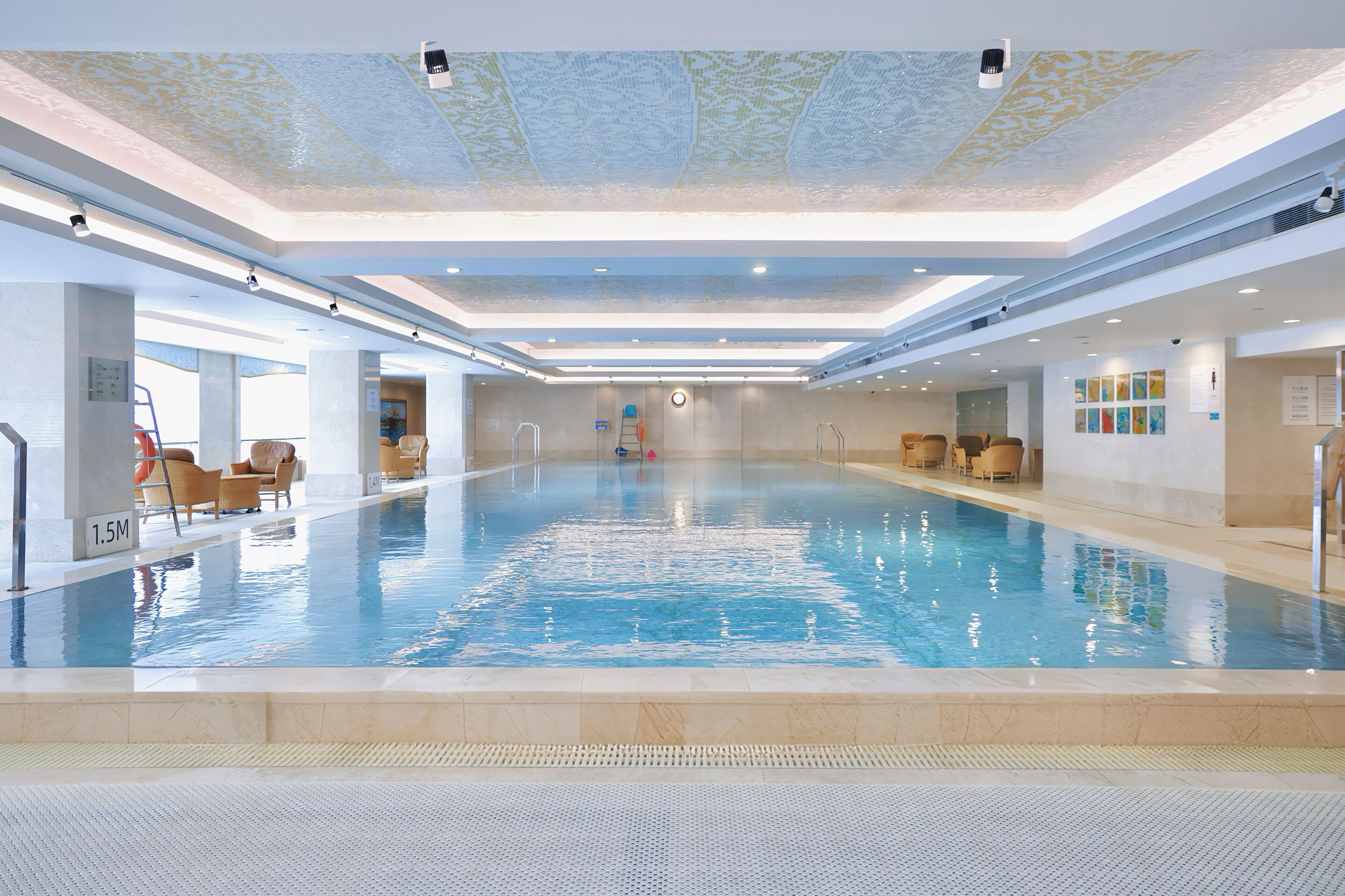 A large indoor swimming pool with clear water, surrounded by lounge chairs and a tiled floor.