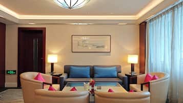 A hotel room with a sofa set, two side tables, a coffee table, a chandelier, a framed picture on the wall, and a zebra-patterned rug.