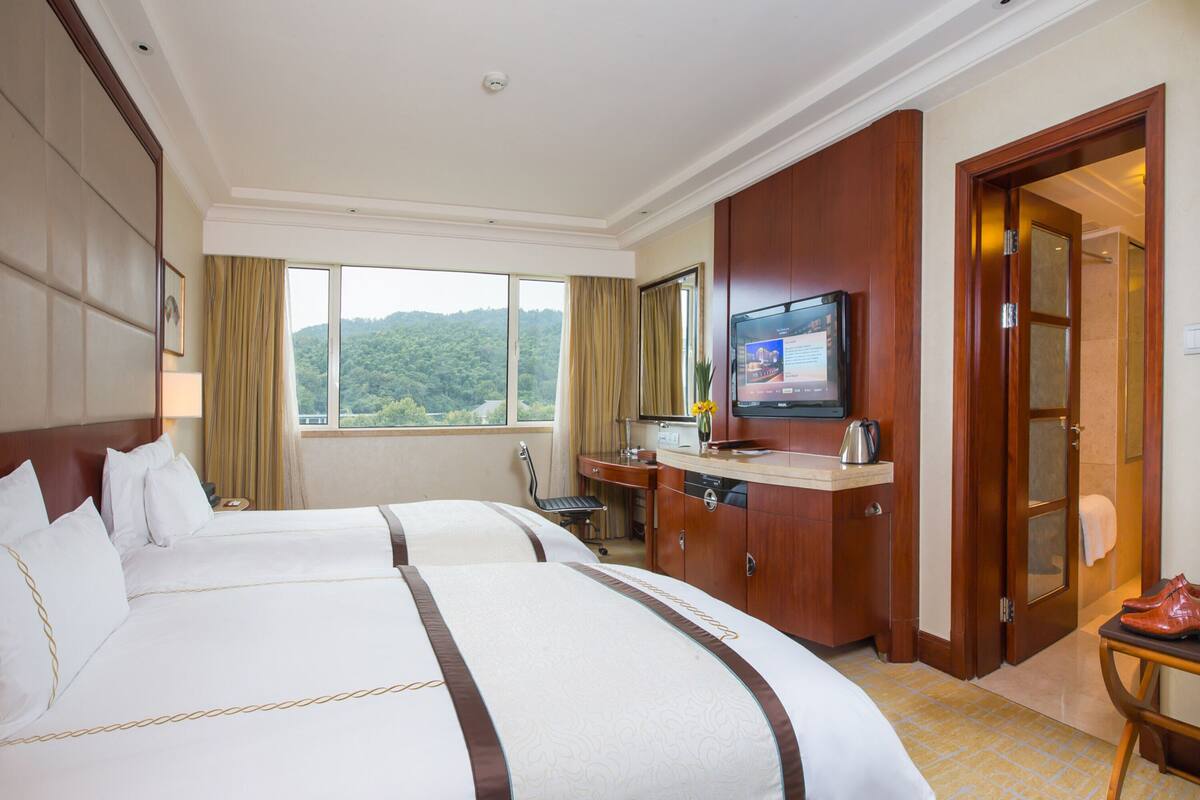 A hotel room with two beds, a TV, a desk with a computer, and a view of the mountains.