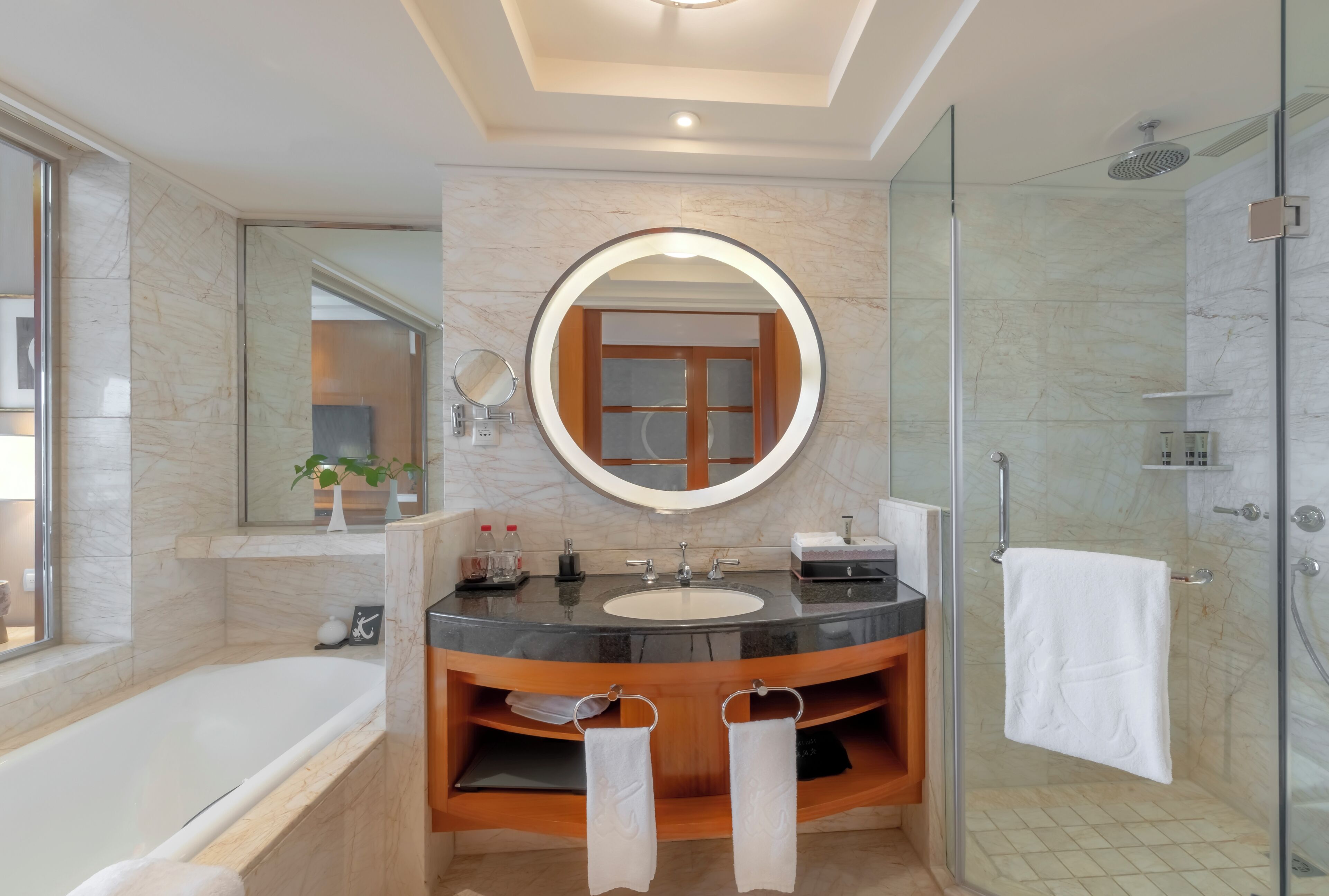 A modern bathroom with a bathtub, a round mirror, a vanity with a sink, and a shower area.