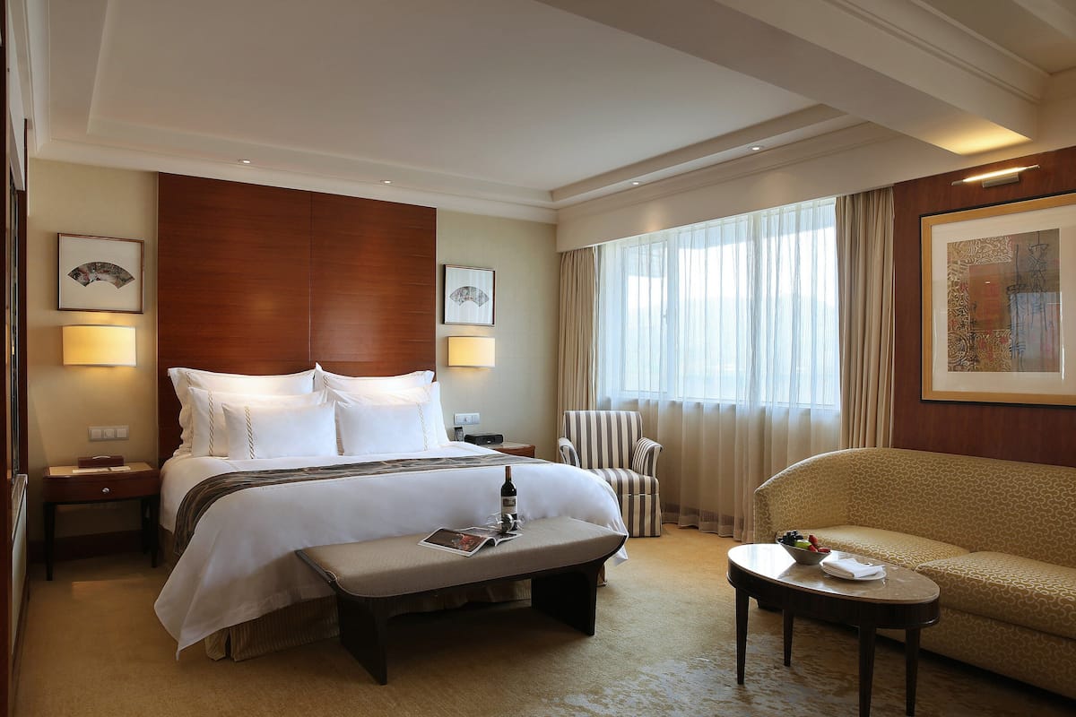 A hotel room with a large bed, a bedside table, a chair, a small table, and a window with curtains.