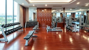 A modern gym with wooden flooring, various exercise equipment, and large windows offering a view of the city. - The Dragon Hotel (Hangzhou)