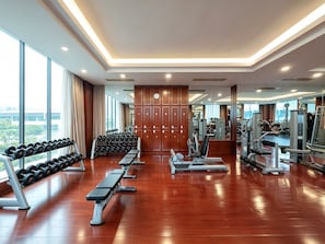 A modern gym with wooden flooring, various exercise equipment, and large windows offering a view of the city.