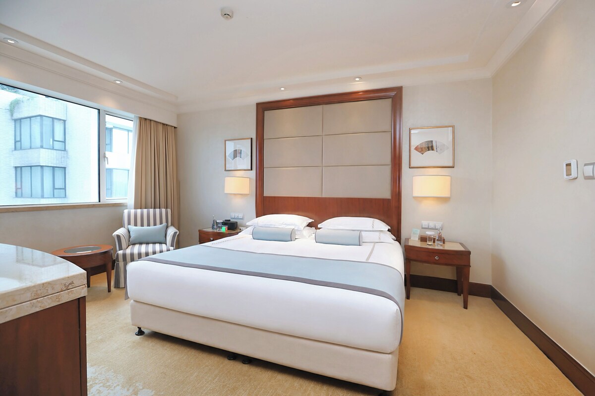 A hotel room with a large bed, a chair, a desk, and a window with curtains.