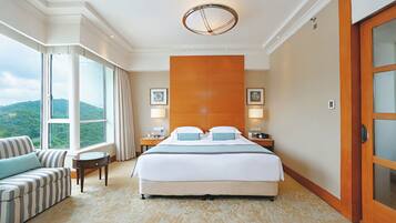A hotel room with a large bed, a sitting area with a sofa, a view of the outdoors through a window, and a wooden door.