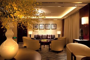 Un hall de hotel con un conjunto de sofás, dos mesas auxiliares, un jarrón grande con flores amarillas y obras de arte enmarcadas en la pared.